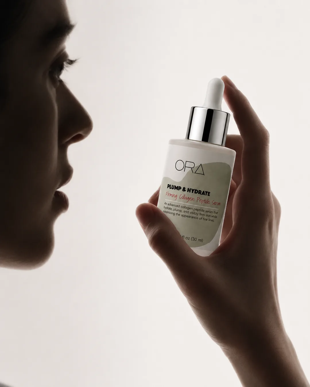 In profile against low light, a hand holds the ORA Peptide Serum.